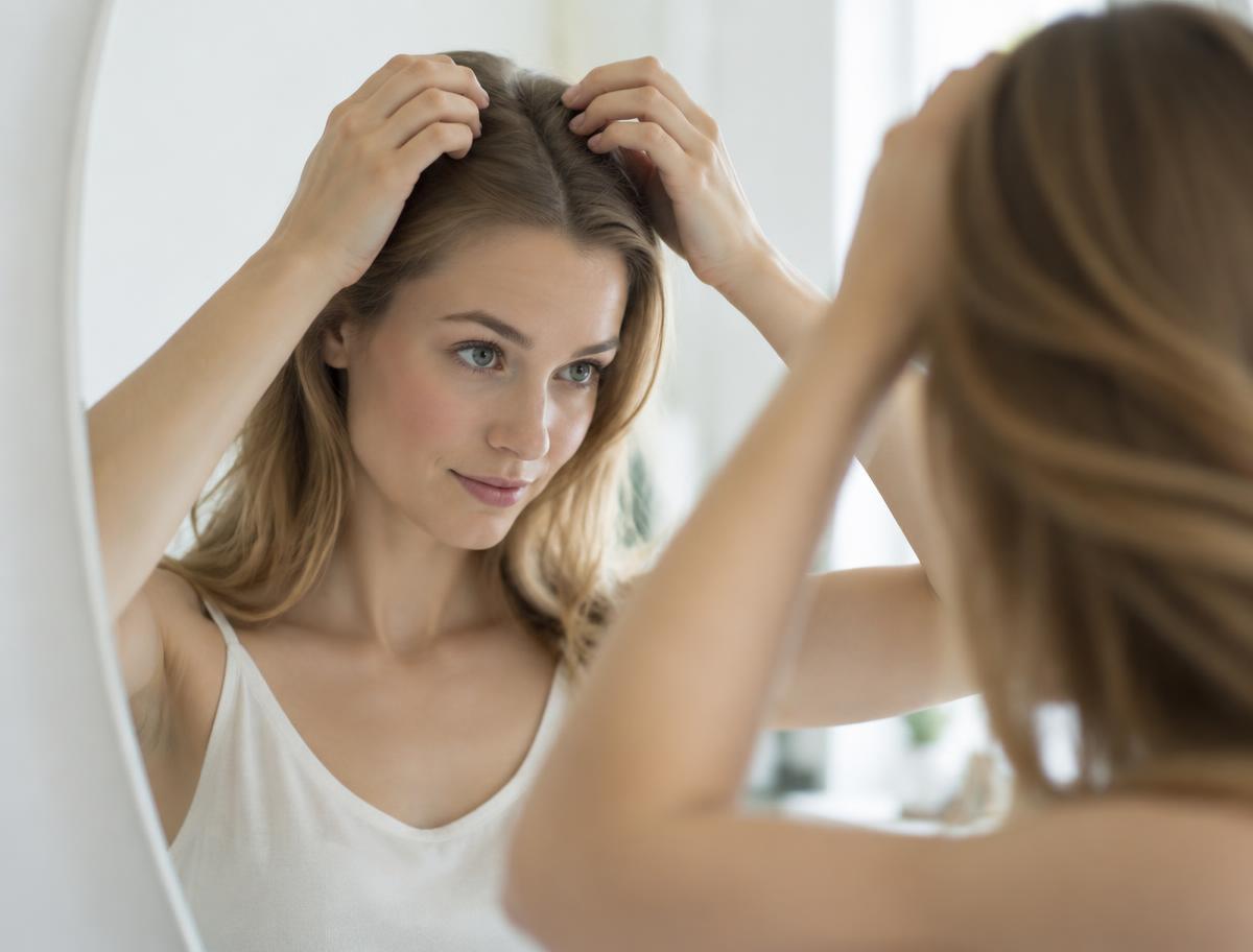 Mujer observando la raya de su cabello frente al espejo
